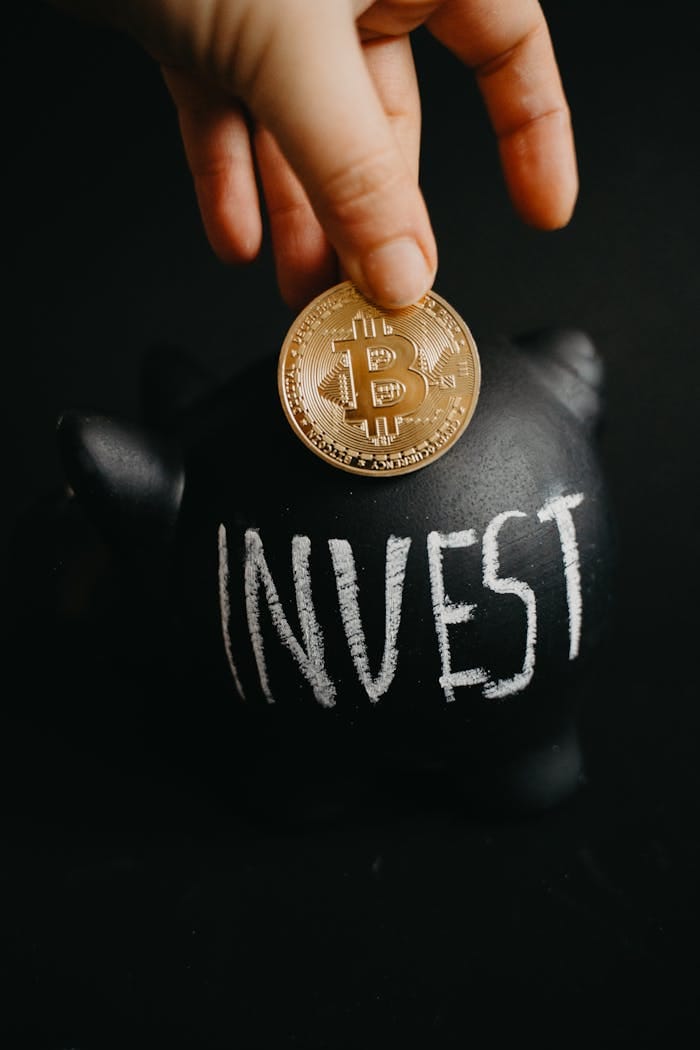 Gold Bitcoin Inserted Into A Black Piggy Bank Labeled 'Invest', Symbolizing Cryptocurrency Saving.
